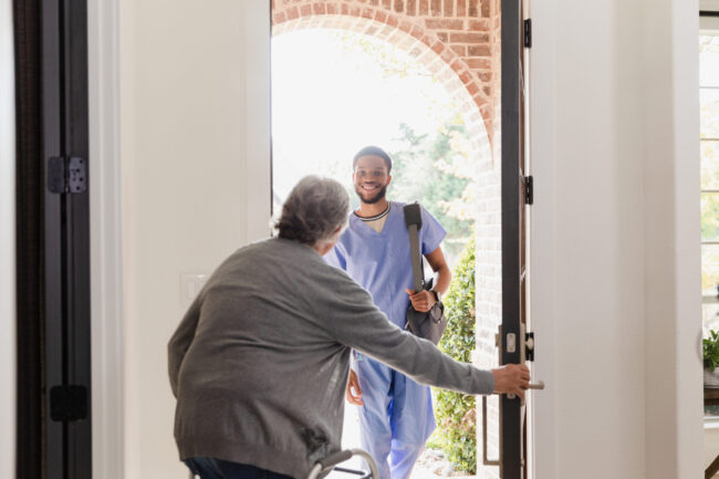 Senior man with walker opens door for physical therapist